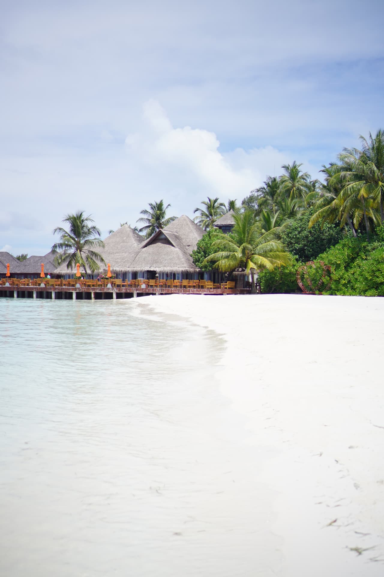 White sand beach and thatched overwater restaurant framed by palm trees in the Maldives