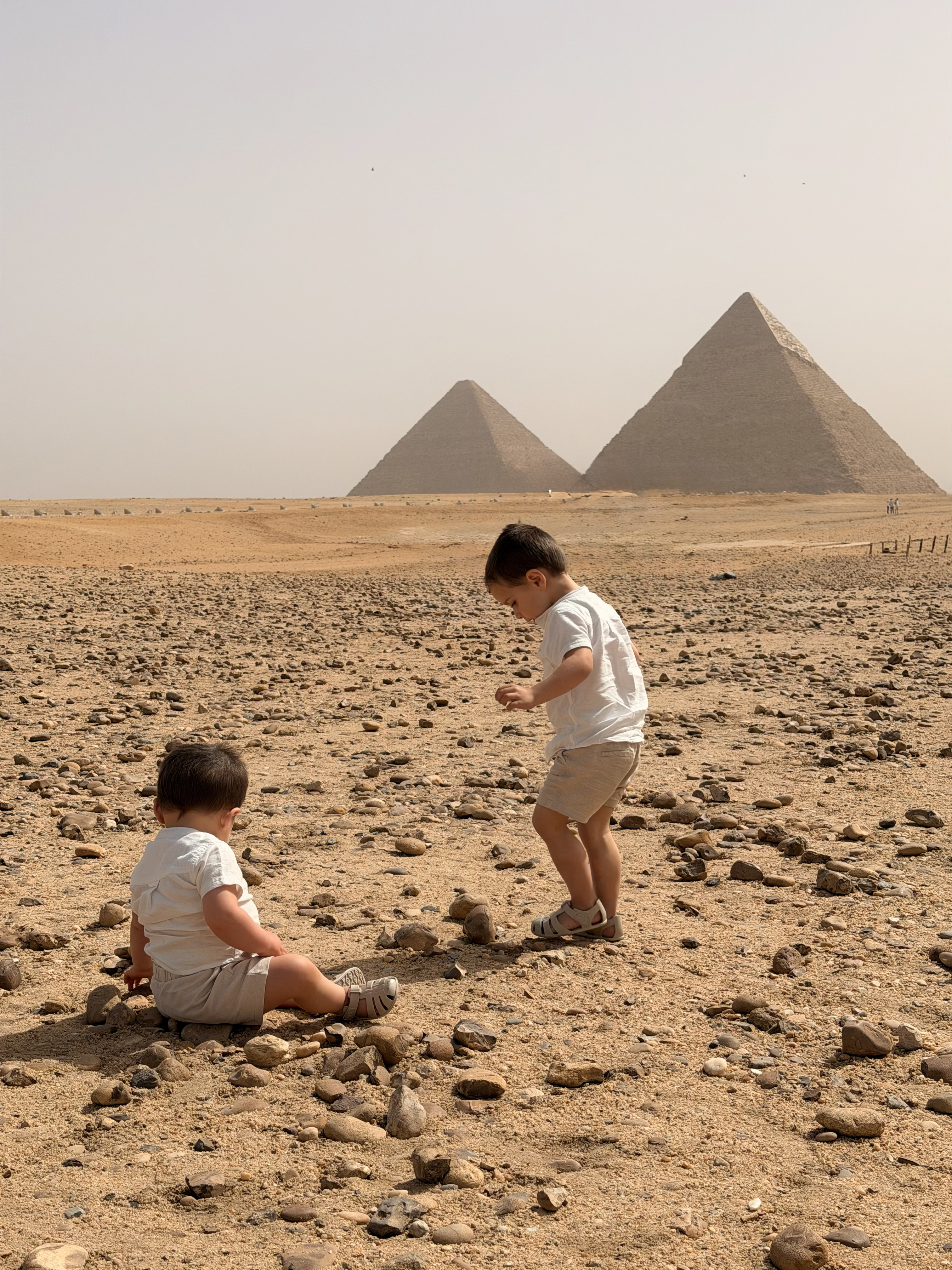 Two small children playing on the sand in front of the Pyramids of Giza