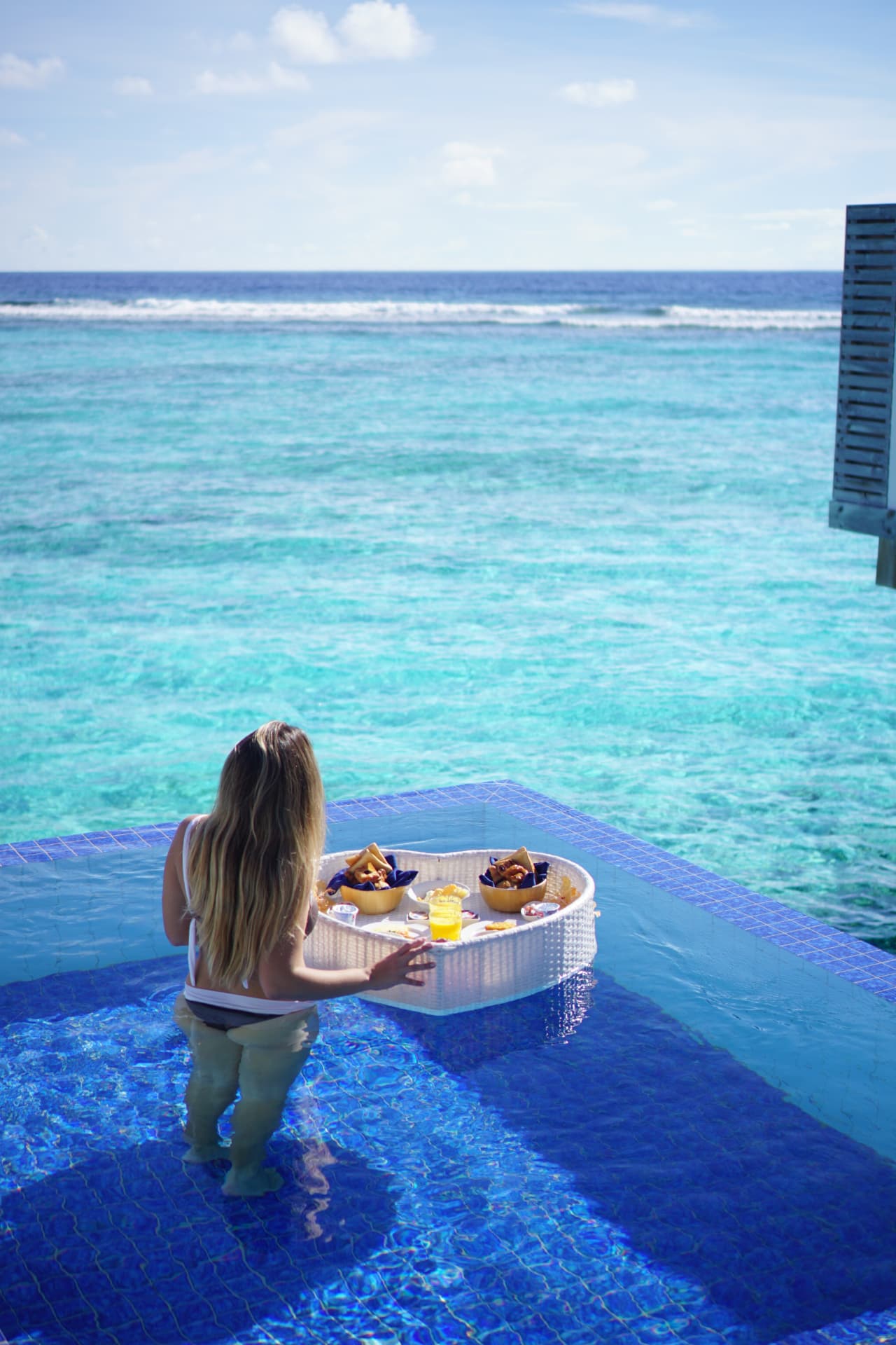 Woman with a heart-shaped floating breakfast in an overwater villa pool facing the ocean