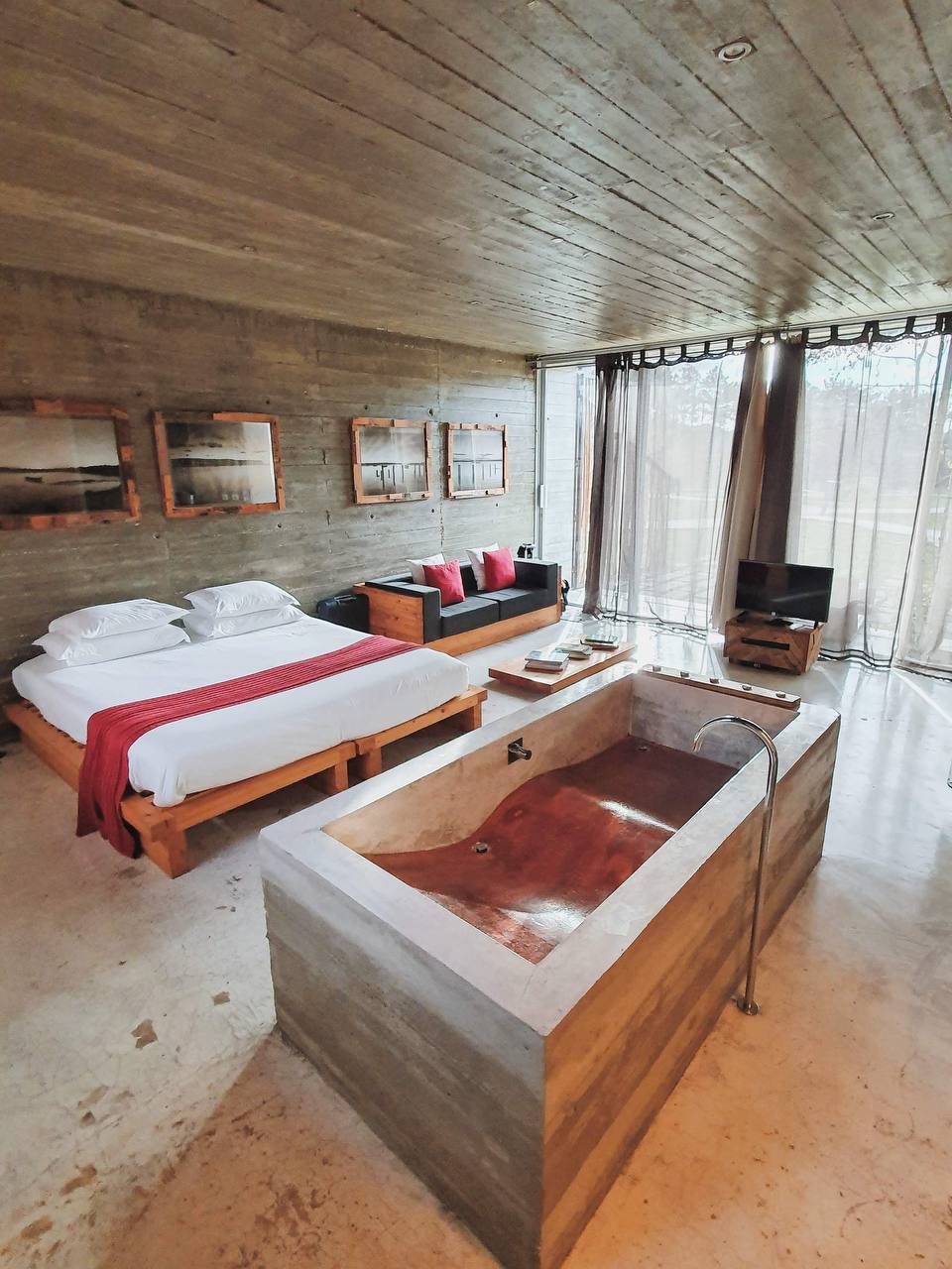 Concrete suite interior with a bed and a freestanding stone bathtub