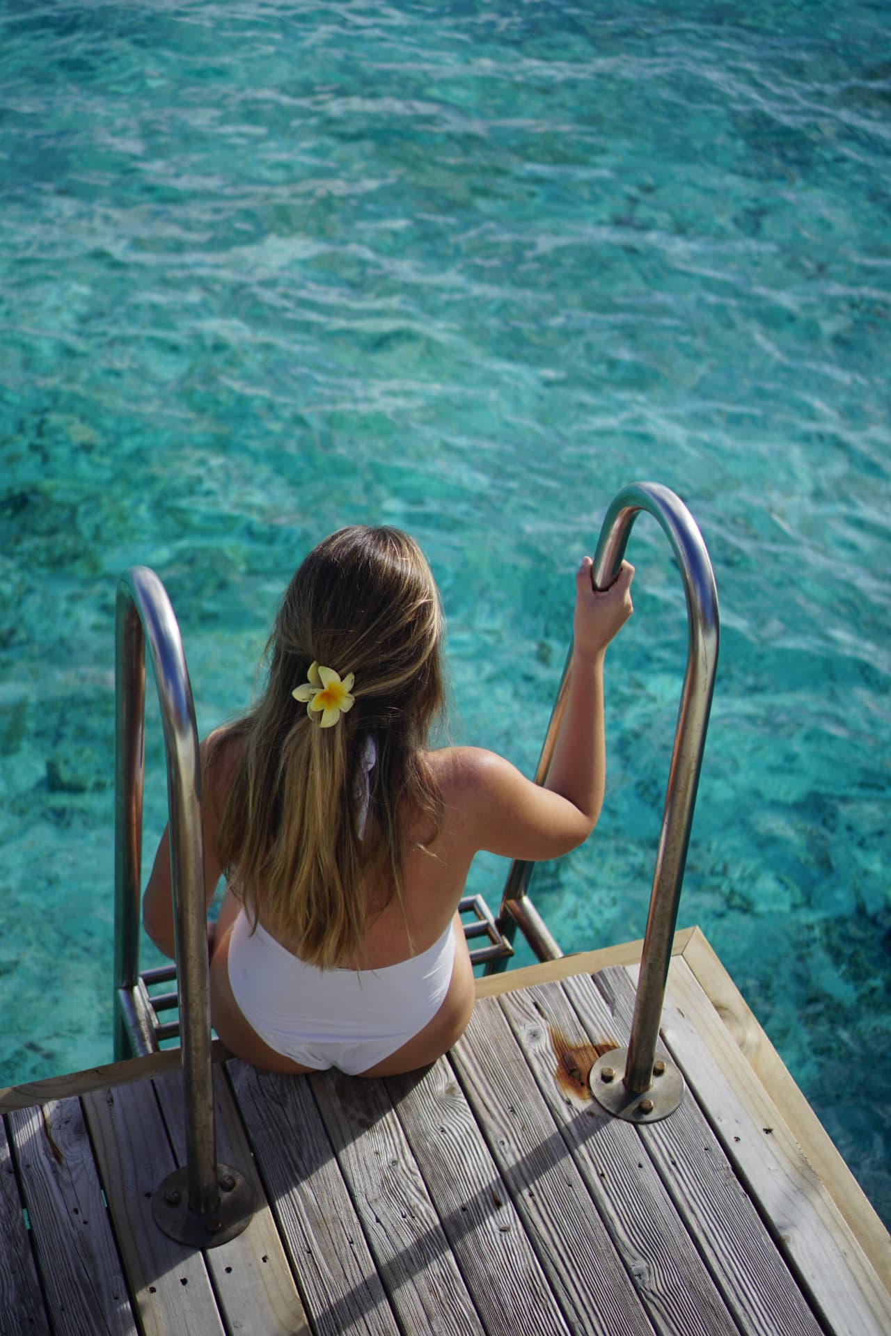 Woman sitting on an overwater villa deck above a clear turquoise lagoon