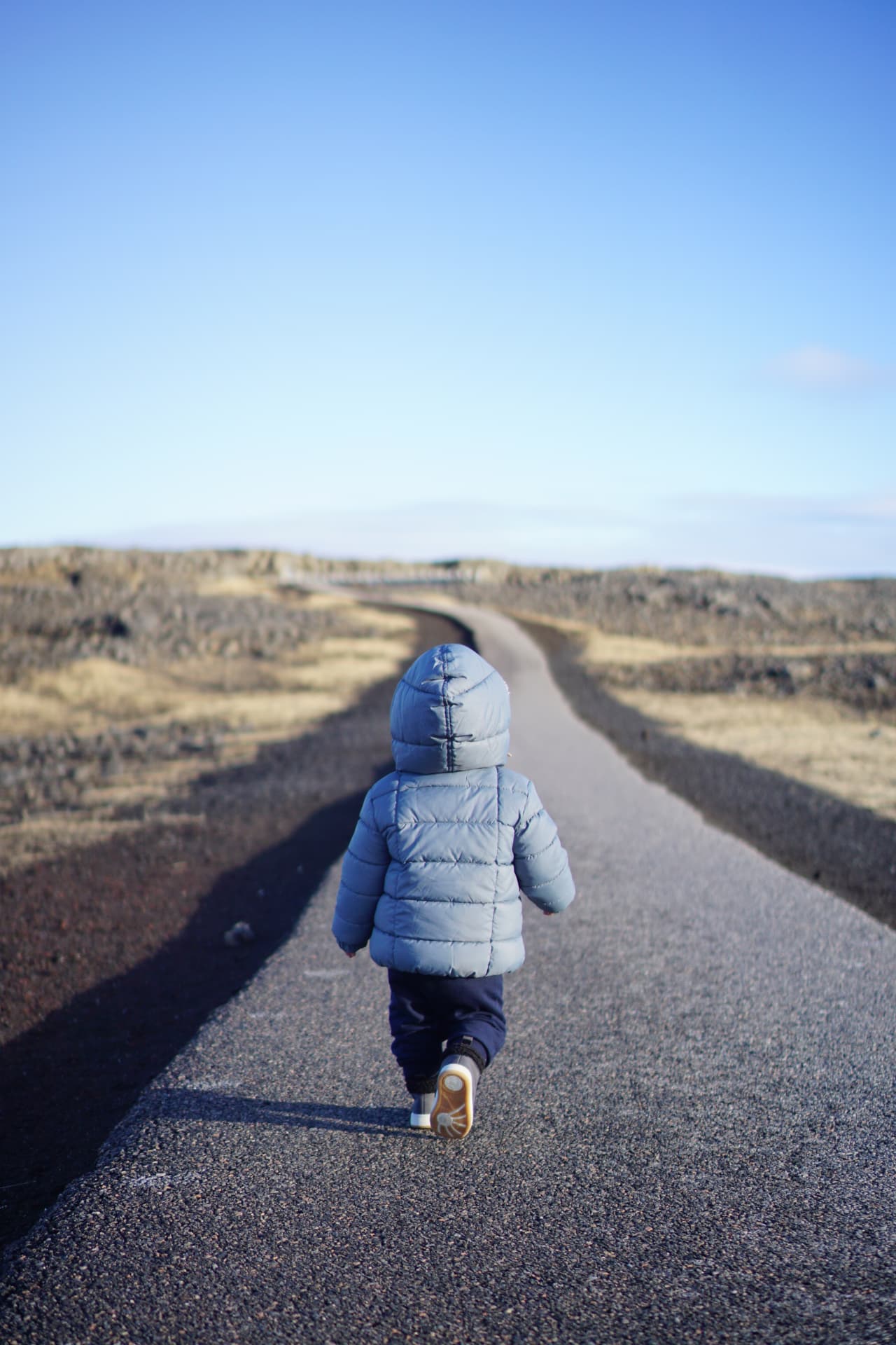 Toddler in a blue coat walking along an empty road through an Icelandic lava landscape