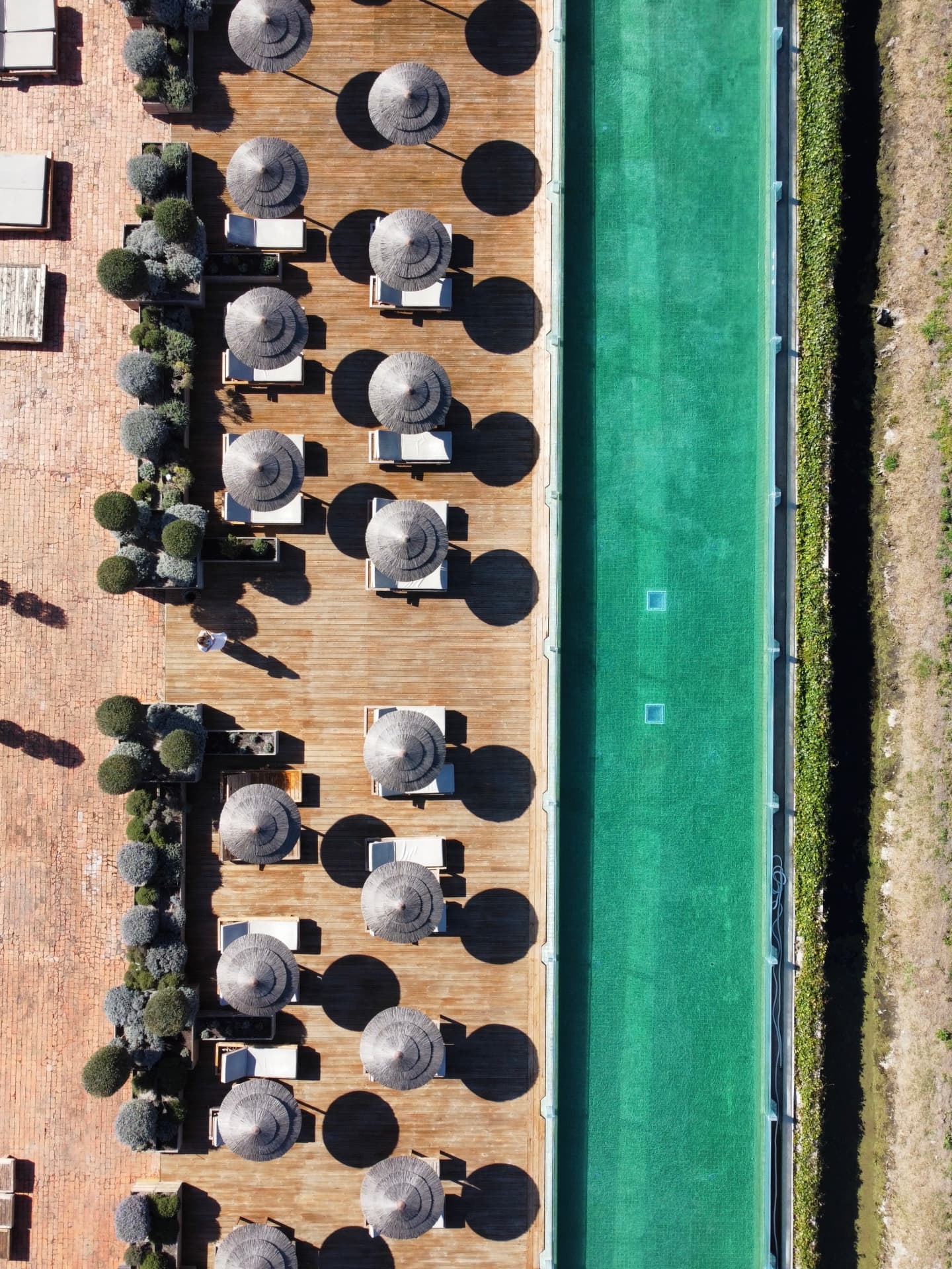 Luxury hotel viewed from above — symmetrical turquoise pool lined with parasols and sunbeds
