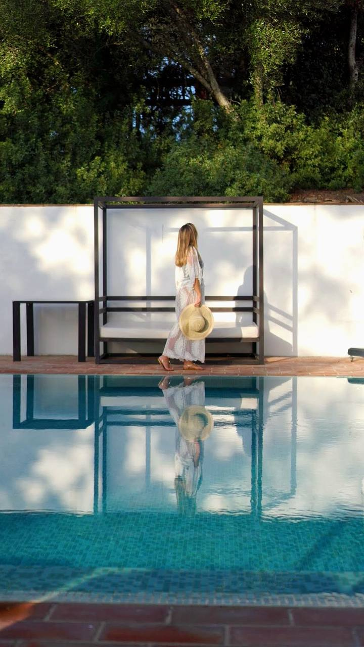 Woman in a white dress walking past a poolside daybed