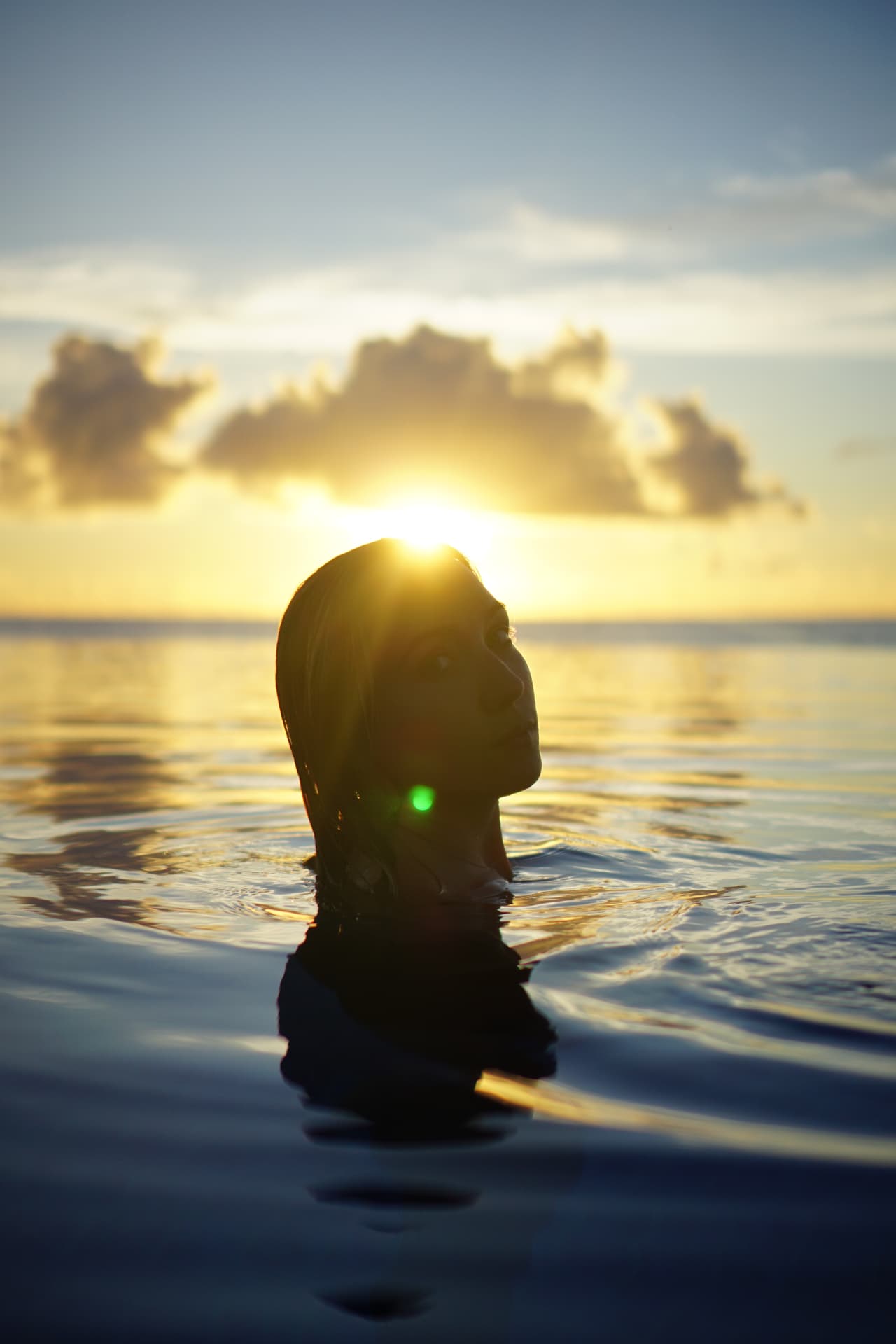 Woman emerging from the sea at sunset, silhouetted against golden light