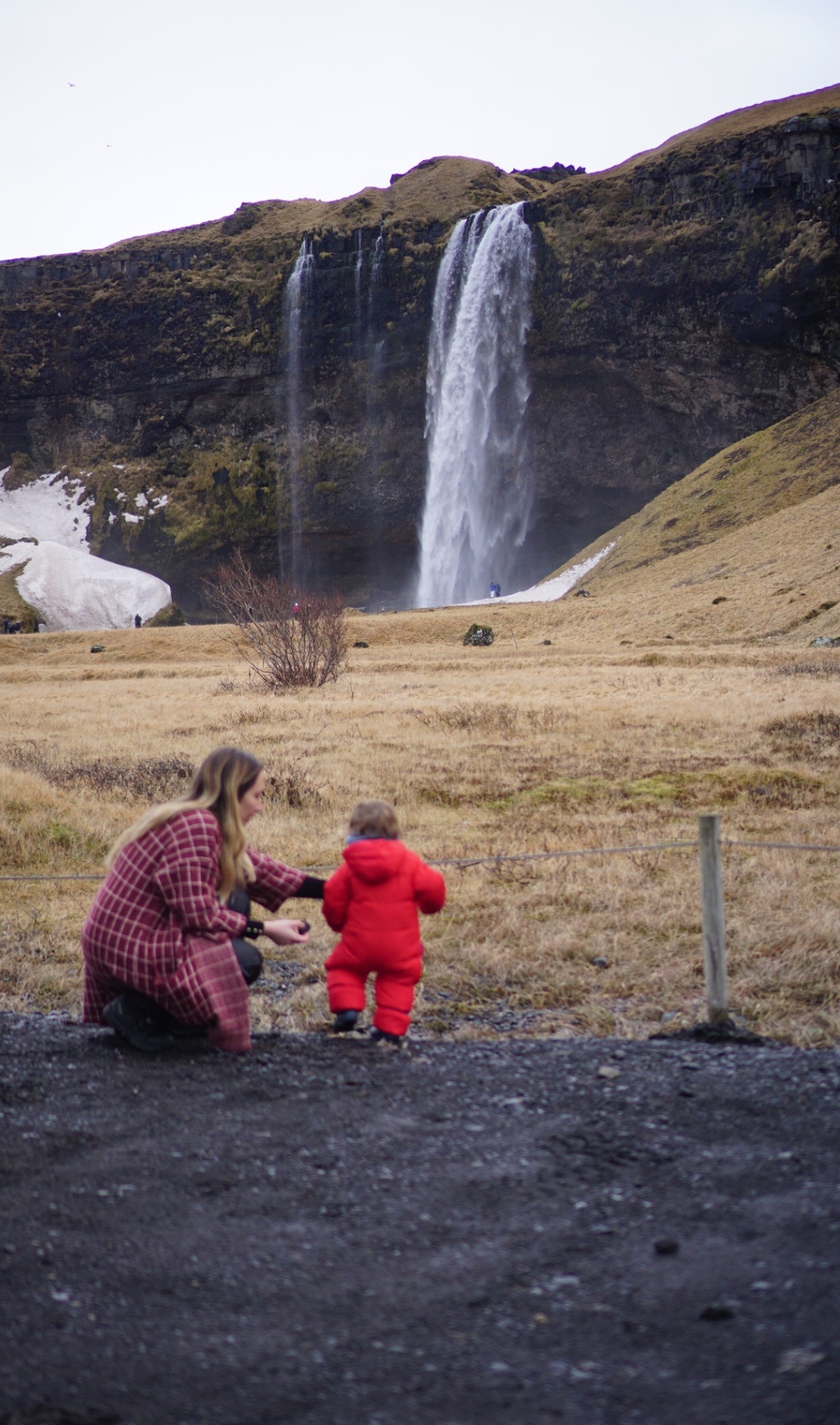 Mother and toddler in a red snowsuit in front of Seljalandsfoss waterfall in Iceland