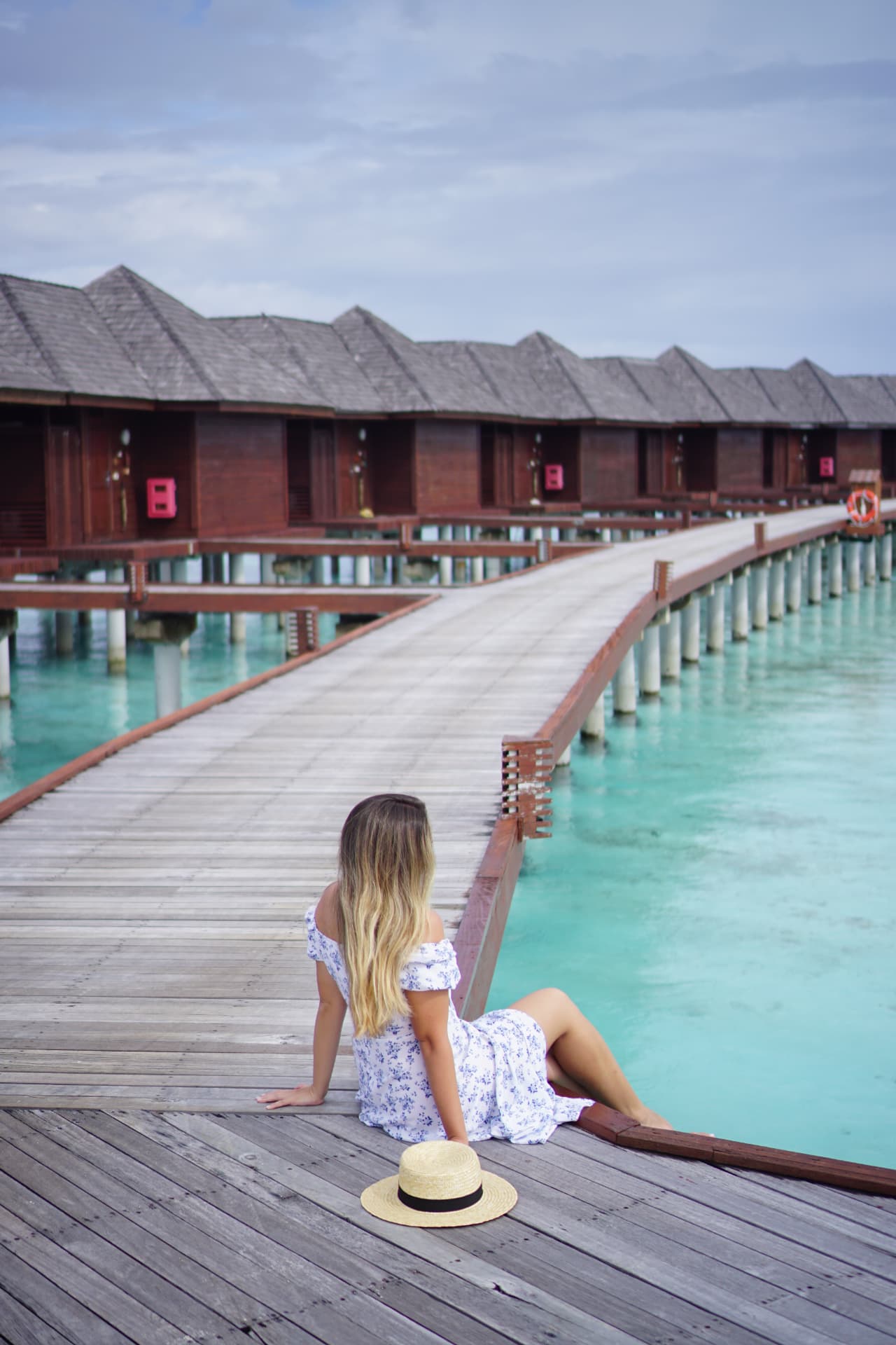 Woman in a floral dress sitting on the wooden jetty beside overwater villas