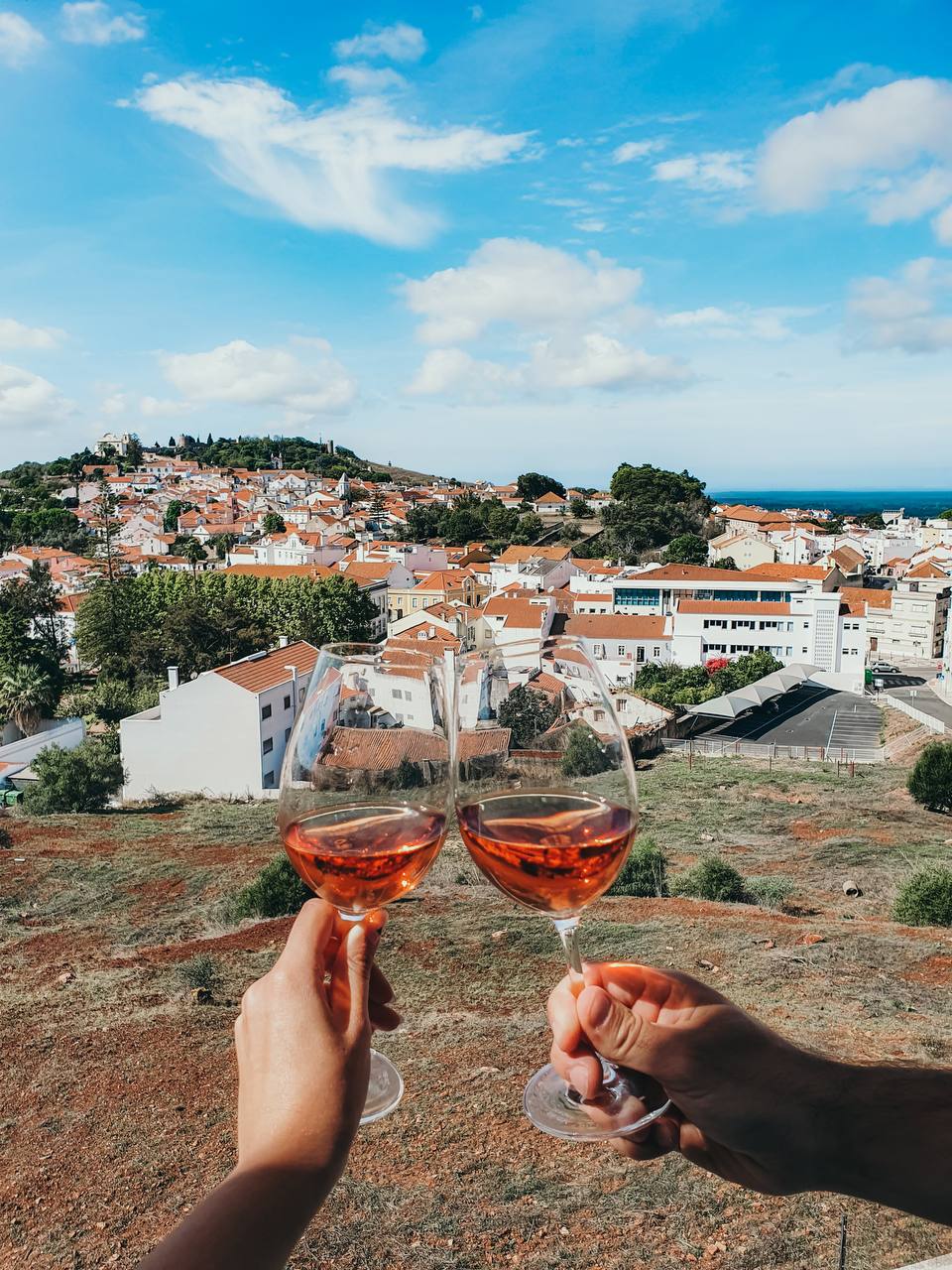 Two glasses of rosé wine raised above a Portuguese hillside town